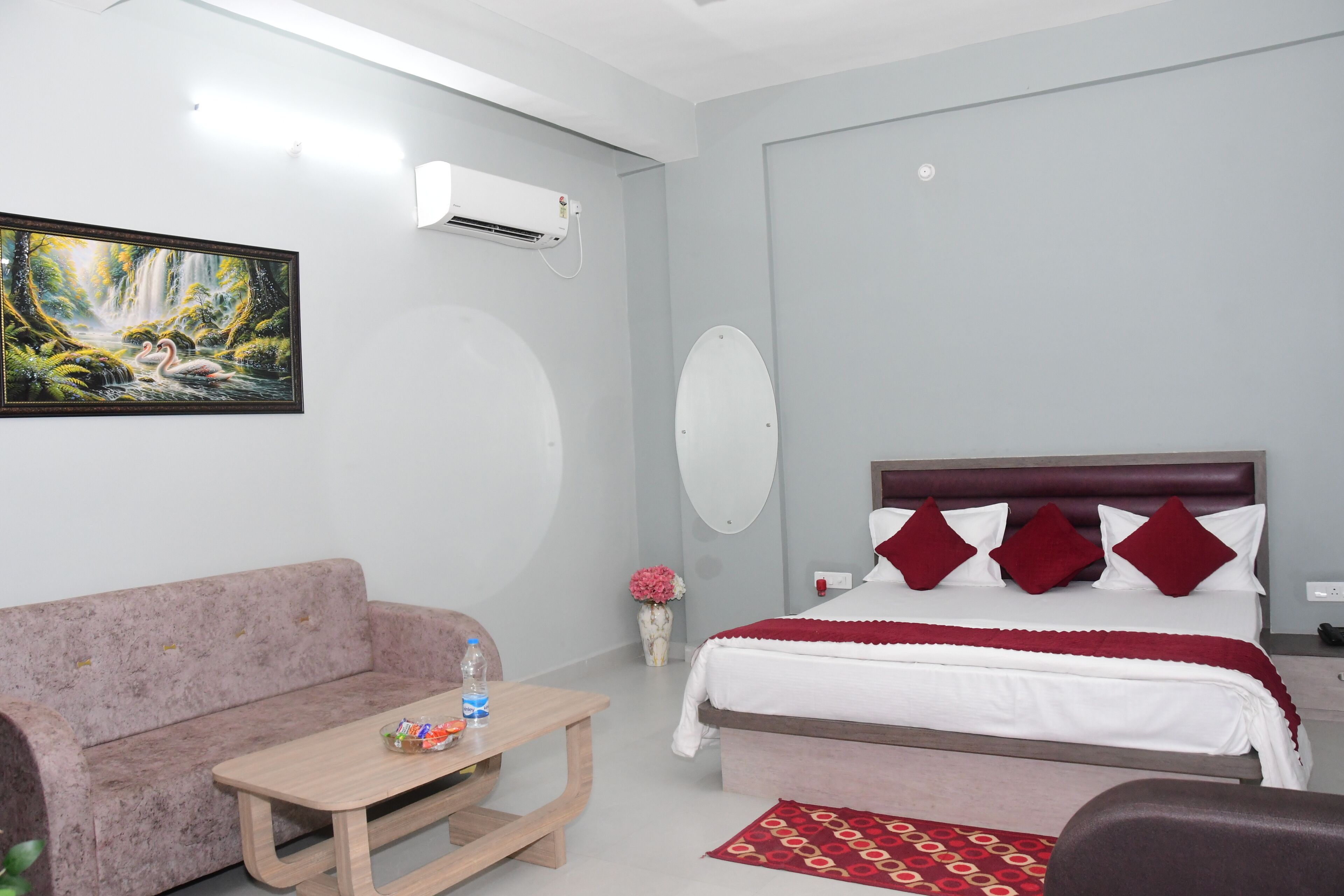 Un dormitorio con cama, sofá, mesa, un cuadro y aire acondicionado.