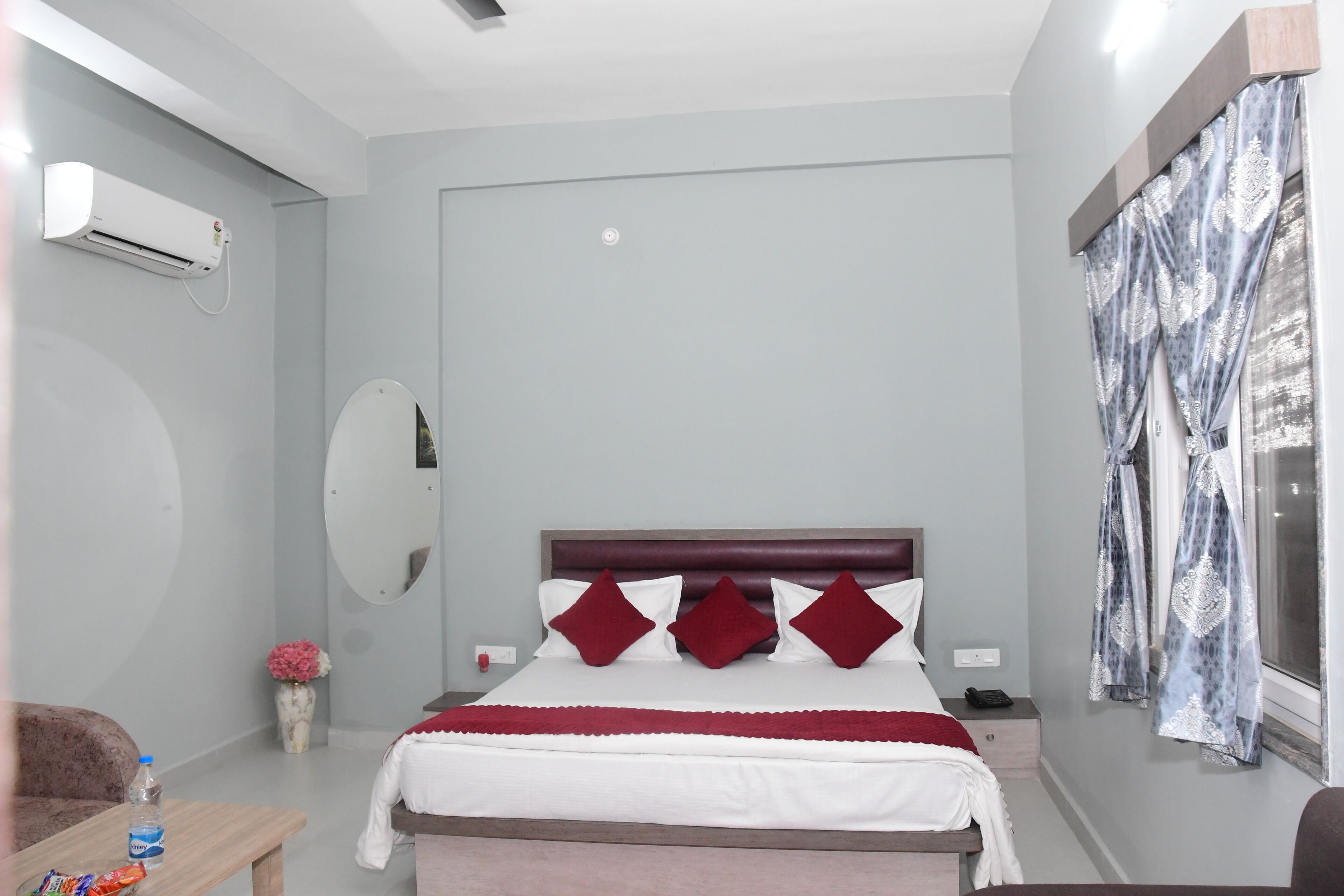 A bedroom with a bed, bedside table, nightstand, and a window with curtains.