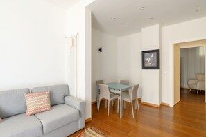 Ein modernes Wohnzimmer mit einer Couch, einem Esstisch mit Glasplatte und einem gerahmten Bild an der Wand.