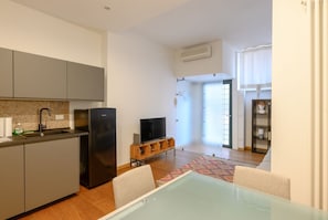 Eine moderne Küche mit grauen Schränken, einem schwarzen Kühlschrank und einem Fernseher auf einem Holzboden.