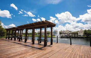 Eine Holzterrasse mit Bänken und einem Gazebo, mit Blick auf ein Gewässer und Häuser im Hintergrund.
