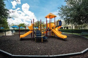 Ein Spielplatz mit Rutschen und Klettergerüsten, umgeben von Bäumen und einem Zaun.