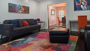 A living room with a sofa, ottoman, colorful rug, and artwork on the walls. - World Cup Ready - Near Downtown & Museum District (Houston)
