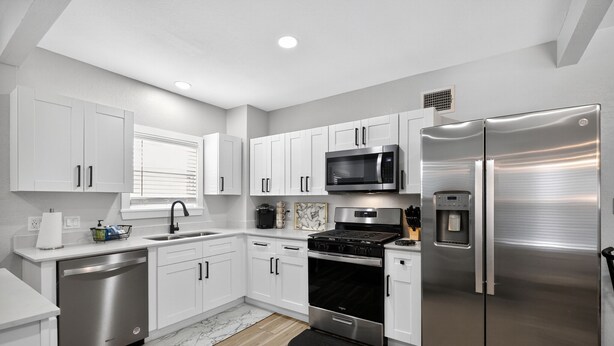A modern kitchen with white cabinets, stainless steel appliances, and a black backsplash. - World Cup Ready - Near Downtown & Museum District (Houston)