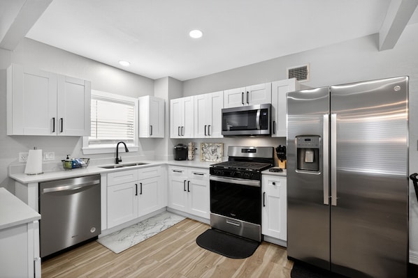 A modern kitchen with white cabinets, stainless steel appliances, and a black backsplash. - World Cup Ready - Near Downtown & Museum District (Houston)