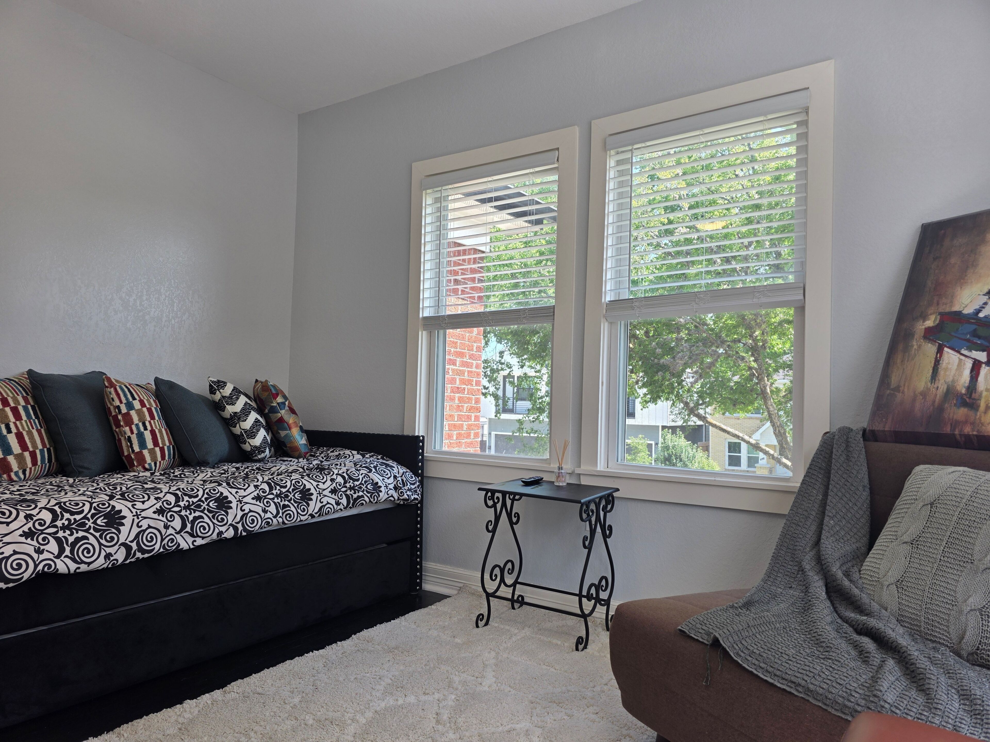 A bedroom with a bed, a small table, and a window with blinds.