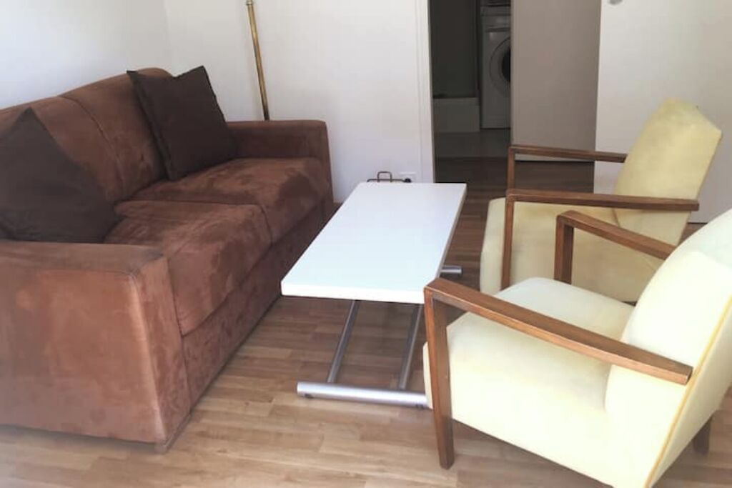 Een woonkamer met een bruine bank, een witte tafel en twee houten stoelen.