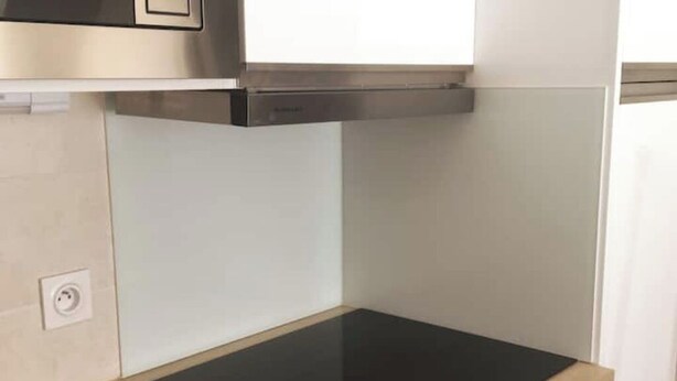 Une cuisine avec un plan de travail noir, une hotte en acier inoxydable et un mur blanc.