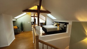 Ein Schlafzimmer im Loft-Stil mit schrägem Dach, einer Holztreppe und Blick auf den angrenzenden Wohnbereich.