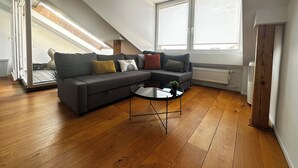 Ein modernes Wohnzimmer mit einer Eckcouch, einem Glastisch, Holzböden und einer schrägen Decke mit Oberlichtern.