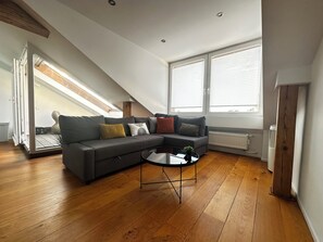 Ein modernes Wohnzimmer mit einer Eckcouch, einem Glastisch, Holzböden und einer schrägen Decke mit Oberlichtern.