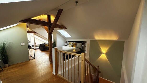 Ein Schlafzimmer im Loft-Stil mit einer Holztreppe, einem Oberlicht und einem Bett mit Kissen.