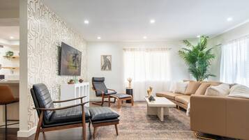 Een moderne woonkamer met een bank, twee fauteuils, een salontafel en een televisie.