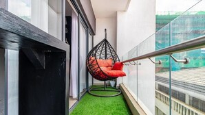 Een balkon met kunstgras, een hangstoel met kussens en een glazen hekwerk.