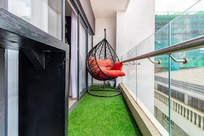A balcony with artificial grass, a hanging chair with cushions, and a glass railing. - Jireh Dwellings Spacious 2Br Comfort with fitness and spacious rooms (Nairobi)