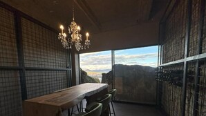 Una habitación con una mesa grande, sillas, una araña y vistas a través de un ventanal.