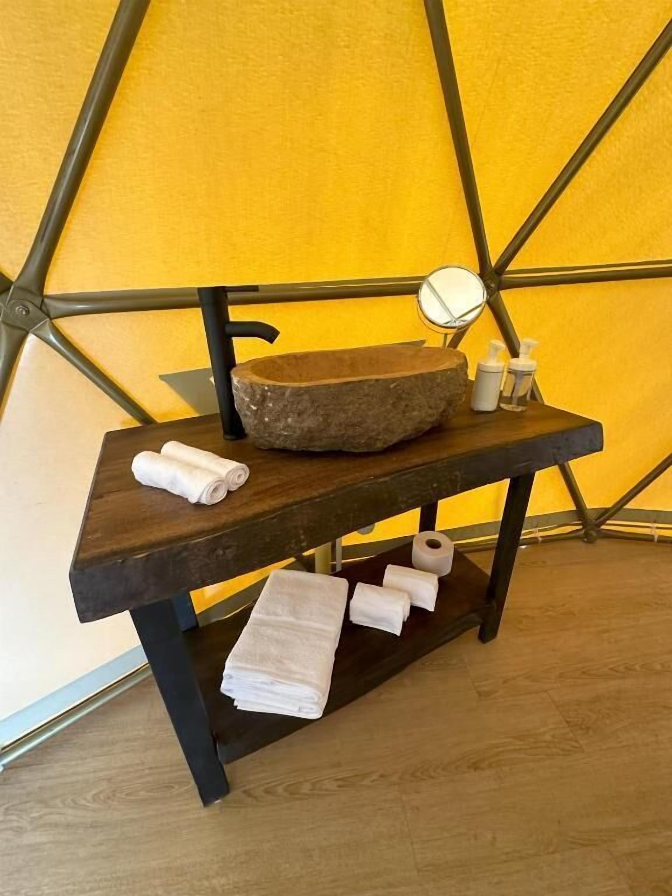 A wooden vanity with a stone basin, a mirror, and toiletries.