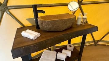 A wooden vanity with a stone basin, a mirror, and toiletries.