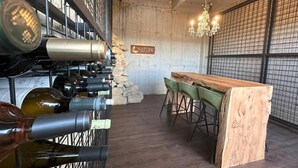 Una cava de vinos con estanterías de madera llenas de botellas, una pared de piedra, una barra de madera con taburetes y un candelabro.