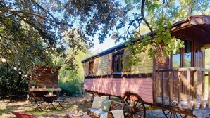A rustic wooden cabin with a porch, a dining table with chairs, and a bench.