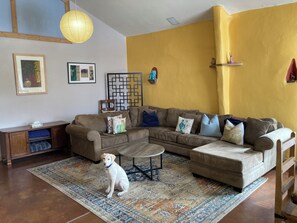 Ein Wohnzimmer mit einem Ecksofa, einem Couchtisch, einem Hund, einem gemusterten Teppich und einer Wandverkleidung.