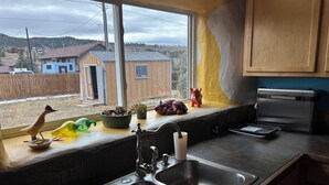 Ett kök med en dubbel diskho, ett fönster med utsikt över hus och diverse köksredskap på fönsterbrädan.
