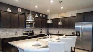 A modern kitchen with dark wood cabinets, stainless steel appliances, and a granite countertop. - Brand New 10BR 8BA/Themed BR/PrivatePool/SPA 16276 (Clermont)