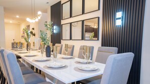 A modern dining room with a long table set for six, grey upholstered chairs, and a contemporary chandelier. - Brand New 10BR 8BA/Themed BR/PrivatePool/SPA 16276 (Clermont)