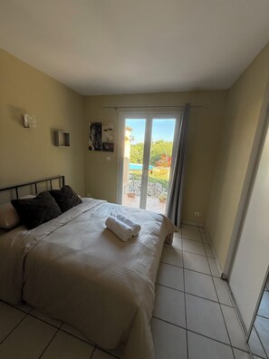 A bedroom with a bed, a view through a sliding glass door, and a tiled floor.