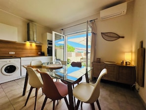A modern kitchen with a glass dining table, chairs, a washing machine, and an air conditioning unit. - - Casa Vista - Panoramic sea view - 50 meters from the beach - (Borgo)