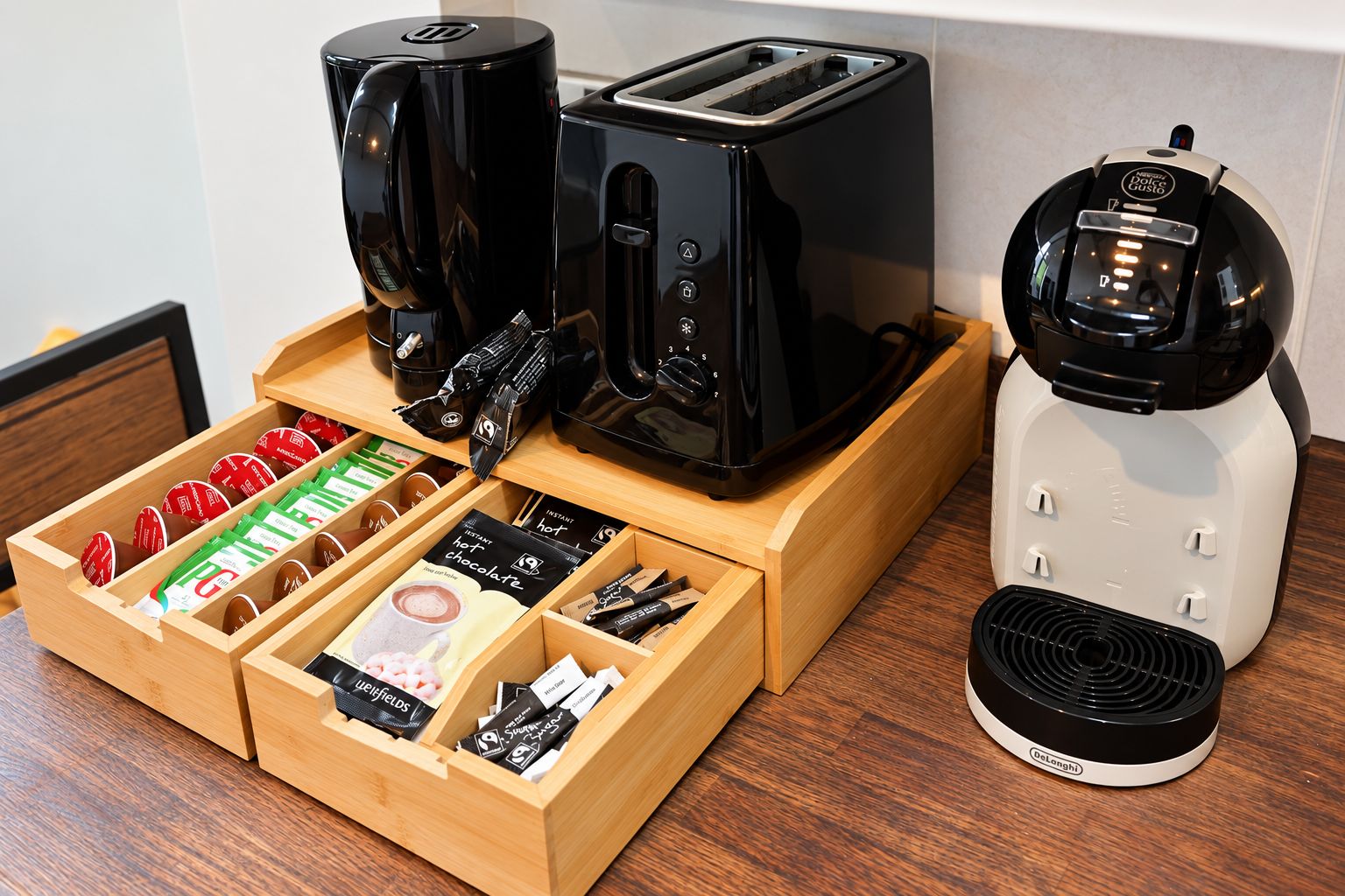 A kitchen area with a coffee maker, toaster, and a drawer containing coffee pods and tea bags.