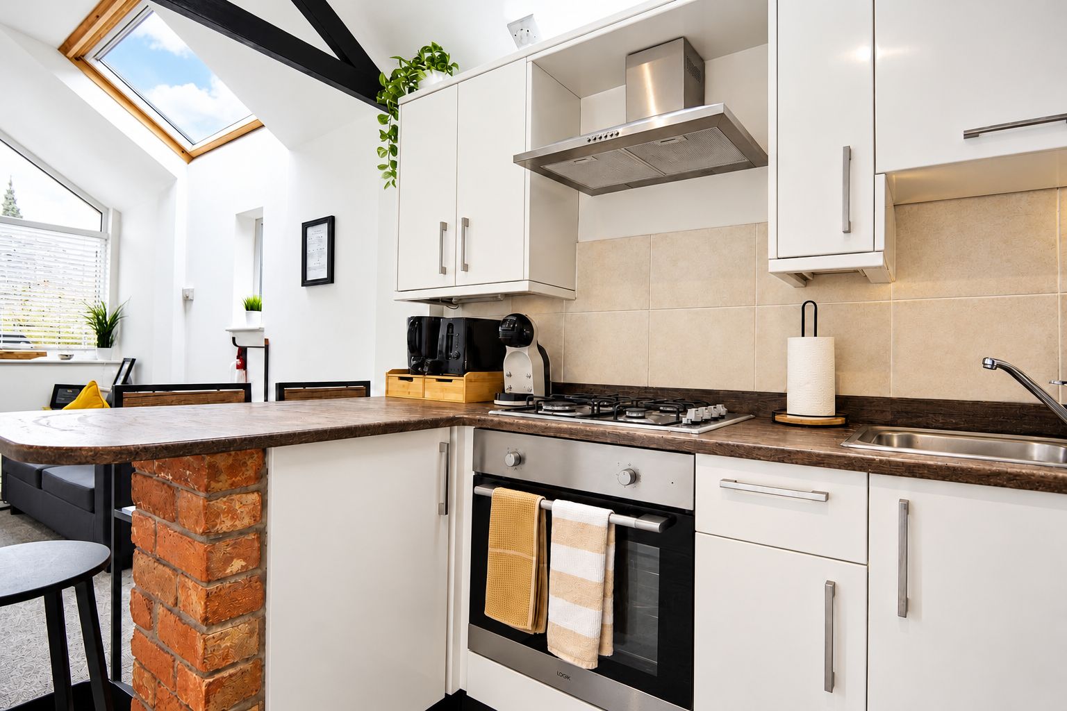 Une cuisine moderne avec des meubles blancs, un mur d’accent en briques, une lucarne et une cuisinière à gaz.