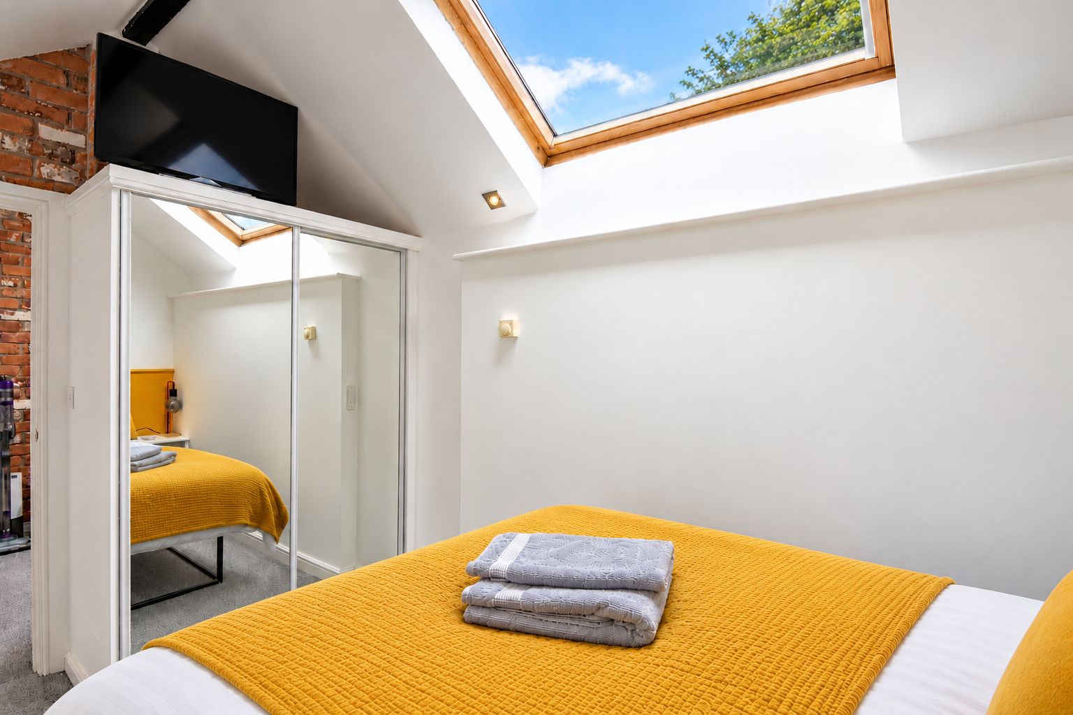 A bedroom with a bed, a wardrobe, a television, and a skylight.