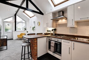 A modern kitchen with a central island, a gas stove, and a built-in oven. There is a skylight above the island and a view of the outside through large windows. - Bright And Airy Cottage Close To Salisbury Centre (Salisbury)