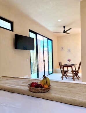 Ein Hotelzimmer mit einem Bett, einem Obstkorb, einem an der Wand befestigten Fernseher und einem Essbereich mit Tisch und Stühlen.