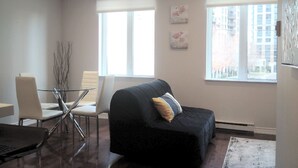 A modern living room with a black sofa, a glass coffee table, and white chairs. - Cozy Fully Furnished Apt w/ Parking (Toronto)
