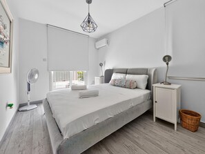 Ein modernes Schlafzimmer mit Bett, Nachttisch, Lampe und einem Standventilator.