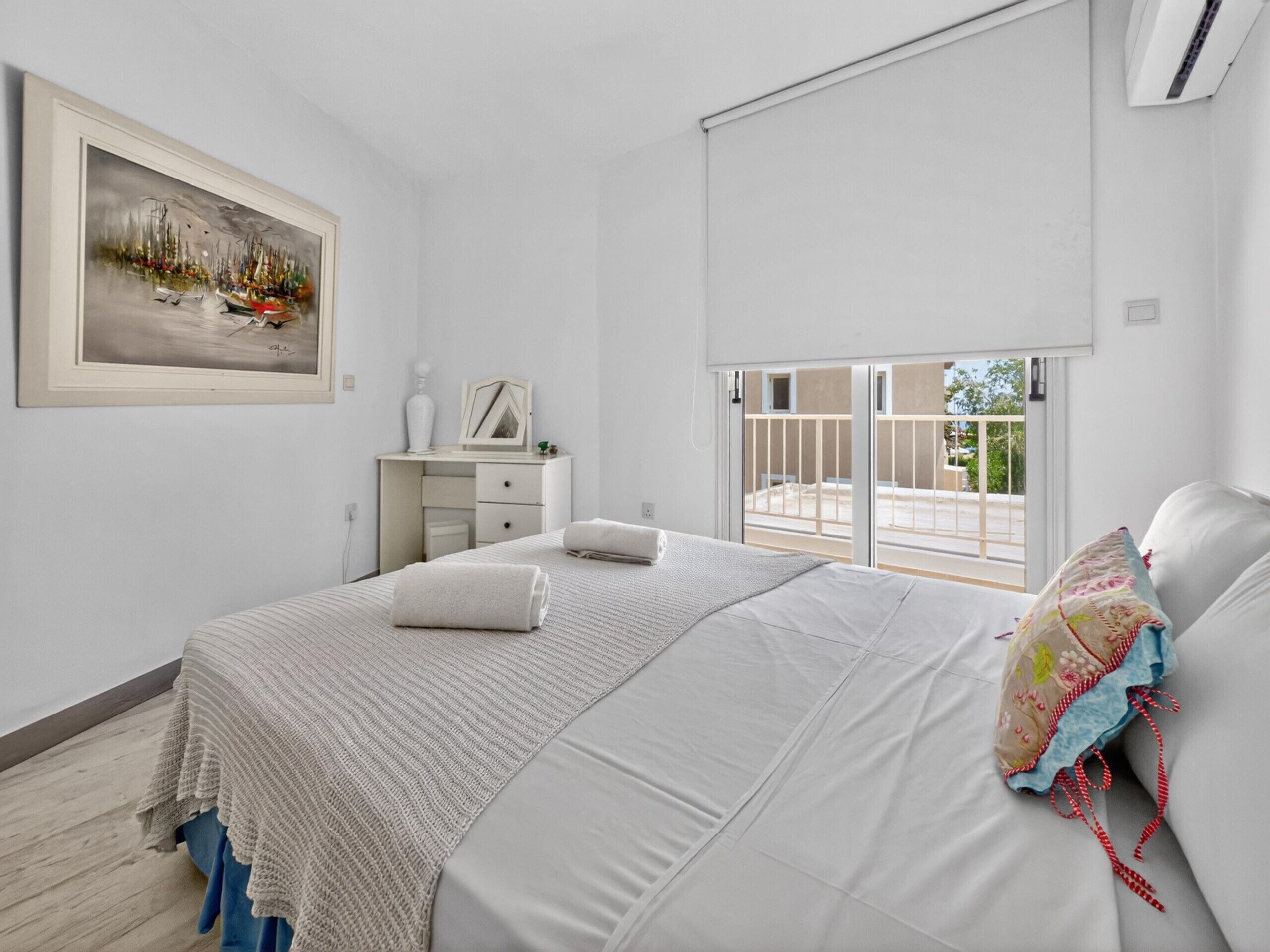 Un dormitorio con cama, escritorio, silla, ventana y un cuadro.