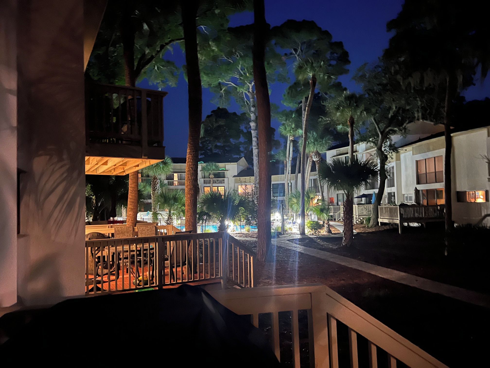 A nighttime view of a resort with multiple buildings, a pool area, and a wooden deck.