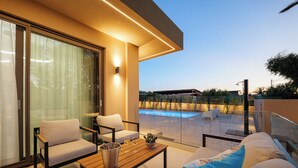A modern outdoor seating area with a pool, a wooden table, and a sofa. - Verde De Luna Villa (Hersonissos)