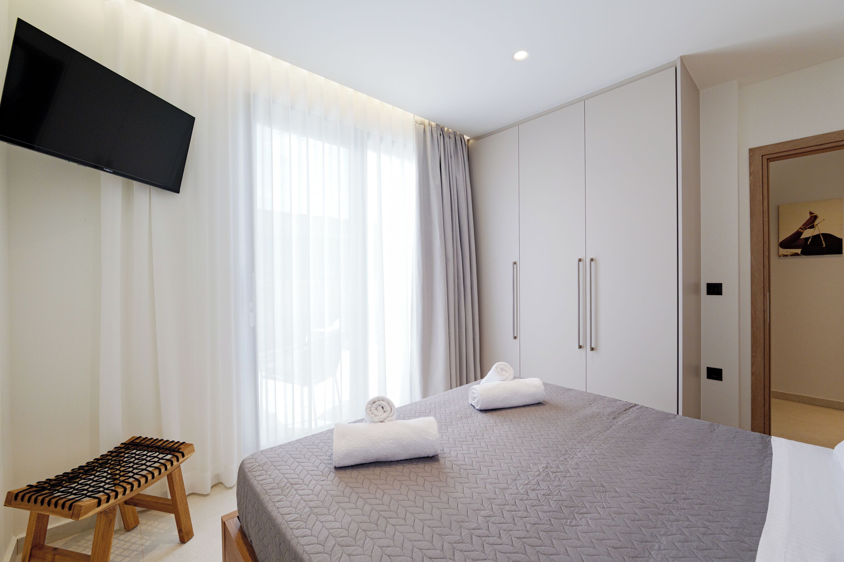 A modern hotel room with a bed, a TV mounted on the wall, and a wardrobe.