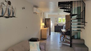 A modern living room with a sofa, a small table, a lamp, and a staircase leading to a kitchen area. - Gîte des Tamarins - Saint-Pierre la Mer - Aude (Fleury)