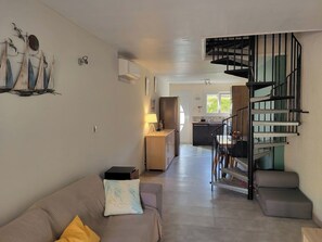 Ein modernes Wohnzimmer mit einer Couch, einem kleinen Tisch, einer Lampe und einer Treppe, die in einen Küchenbereich führt.