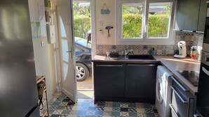 A compact kitchen with a washing machine, a sink, and a window with a view of greenery. - Gîte des Tamarins - Saint-Pierre la Mer - Aude (Fleury)