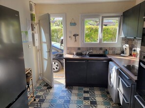 Eine kleine Küche mit Waschmaschine, Spüle und Fenster mit Blick auf Grünflächen.