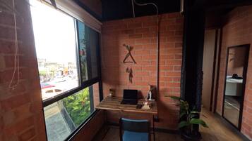 A room with a brick wall, a wooden desk, a chair, a laptop, and a large window.