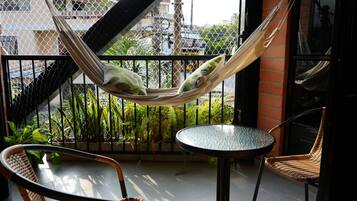 A hammock on a balcony with a view of a city street, a round table, and wicker chairs.