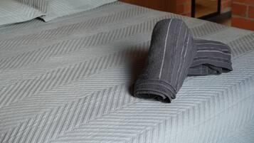 A bed with a patterned bedspread, a wooden door, and a brick wall.