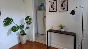 Una habitación con suelo de madera, pared blanca, planta de monstera en maceta, una mesita con lámpara y dos obras de arte abstracto enmarcadas.