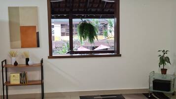 Una habitación con ventana, una estantería, una planta en maceta y una alfombra estampada.